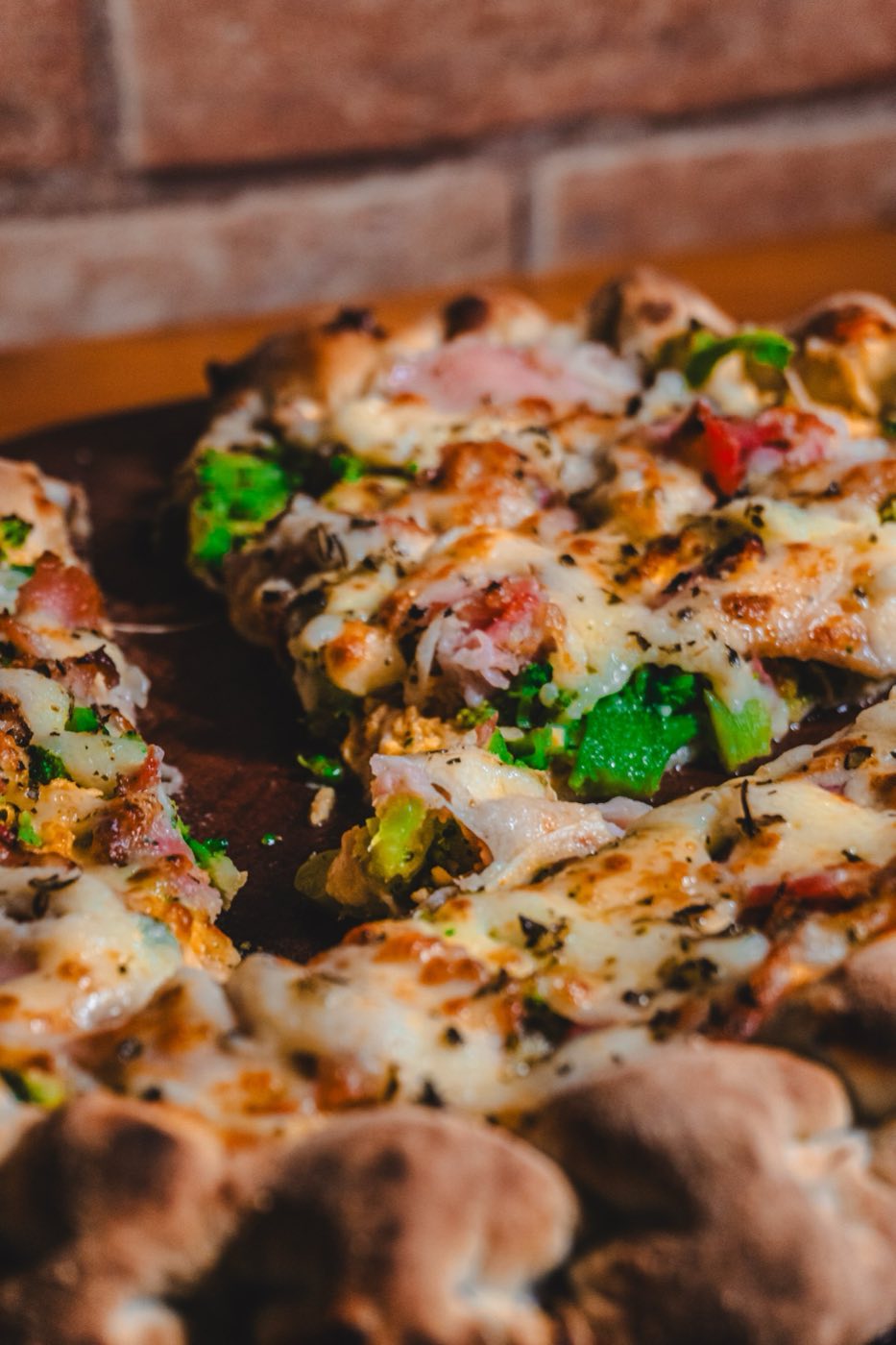 Pizza da Giacomin fatiada na pedra, com a parede de tijolo da casa ao fundo